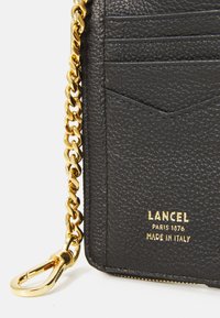 Fekete textúrájú bőr pénztárca arany lánccal és csattal; kártyatartókat és dombornyomott logót tartalmaz: "LANCEL PARIS 1876 MADE IN ITALY."