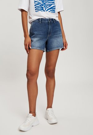 Denim shorts in a medium blue wash with a relaxed fit, frayed hem, and classic five-pocket styling. Pairing with a white graphic t-shirt.