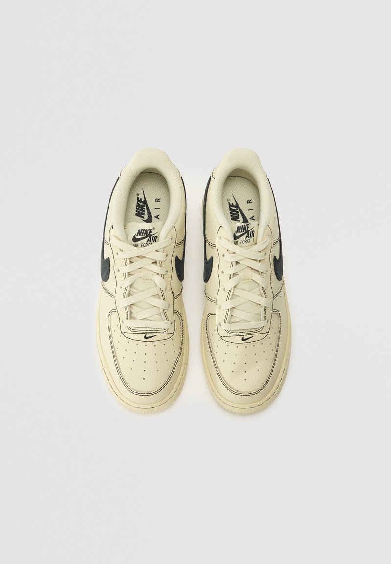 Sneakers Nike Air Force 1 w kremowej skórze z czarnymi akcentami, z perforowanym noskiem, płaskimi sznurowadłami i gumową podeszwą.