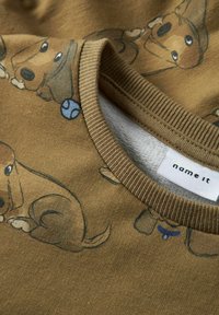 Bruine katoenen shirt met een patroon van geïllustreerde honden, voorzien van een ribbelkraag en een klein blauw baldetail. Merkenlabel zichtbaar.