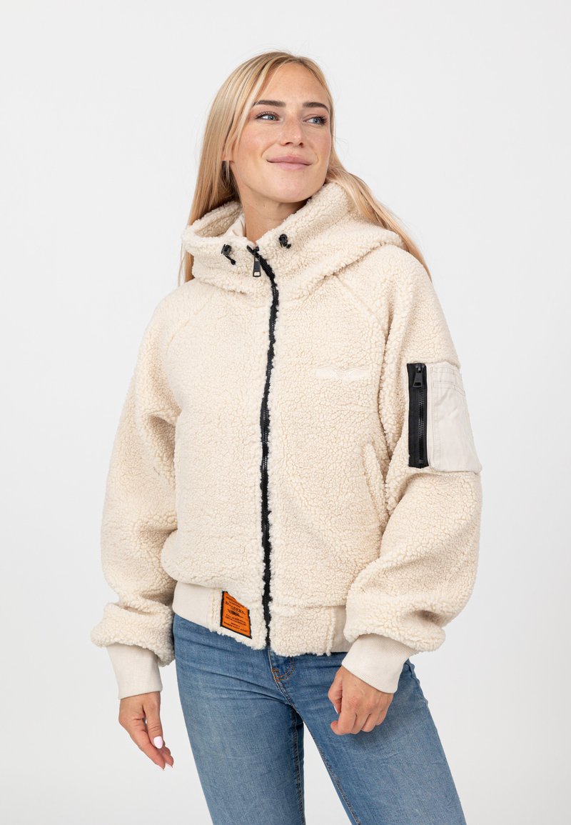 Kremowa polarowa kurtka z czarnym zamkiem błyskawicznym, oversize'owy kaptur, elastyczne mankiety i boczna kieszeń. Posiada teksturowany materiał i pomarańczową metkę.