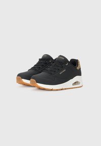 Black athletic sneakers with a textured upper, white midsole, and gum rubber outsole. Features golden branding and a leopard print accent.
