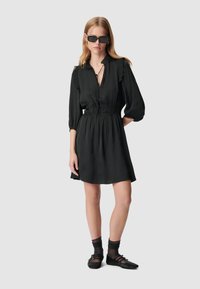 Abito nero con scollatura arricciata, maniche a tre quarti e vita elasticizzata. Un paio di calzini e ballerine completano l'outfit. Texture liscia.