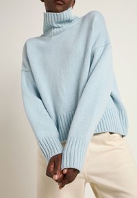 Light blue oversized turtleneck sweater made of soft knit material, featuring ribbed cuffs and hem, with a relaxed fit and textured surface.