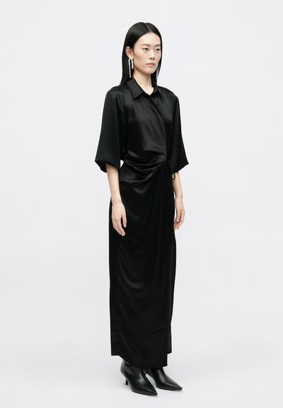 Vestido envolvente preto de cetim com mangas curtas, detalhe de laço lateral e uma silhueta fluida, combinado com botas de tornozelo apontadas pretas.