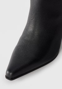 Bottine noire en cuir à bout pointu avec une finition texturée, des bords lisses et un petit talon, présentant un design élégant et minimal.