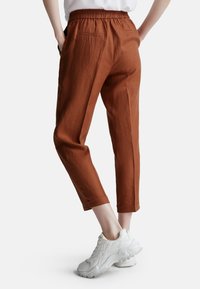 Kalhoty v rustové barvě, lehké, s elastickým pasem, zúženými nohavicemi a bočními kapsami, doplněné o robustní bílé tenisky.