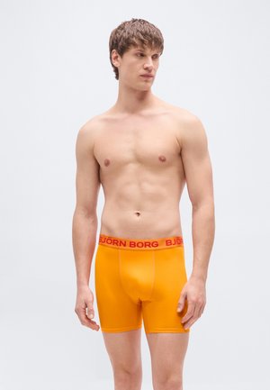 Oranžové boxerky s přiléhavým střihem, s červeným pasem, na kterém je výrazně umístěno logo "BJÖRN BORG". Hladká, elastická látka.