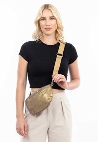 Borsa a tracolla metallica dorata con una texture liscia, forma curva, due scomparti con zip e una tracolla regolabile color tan.