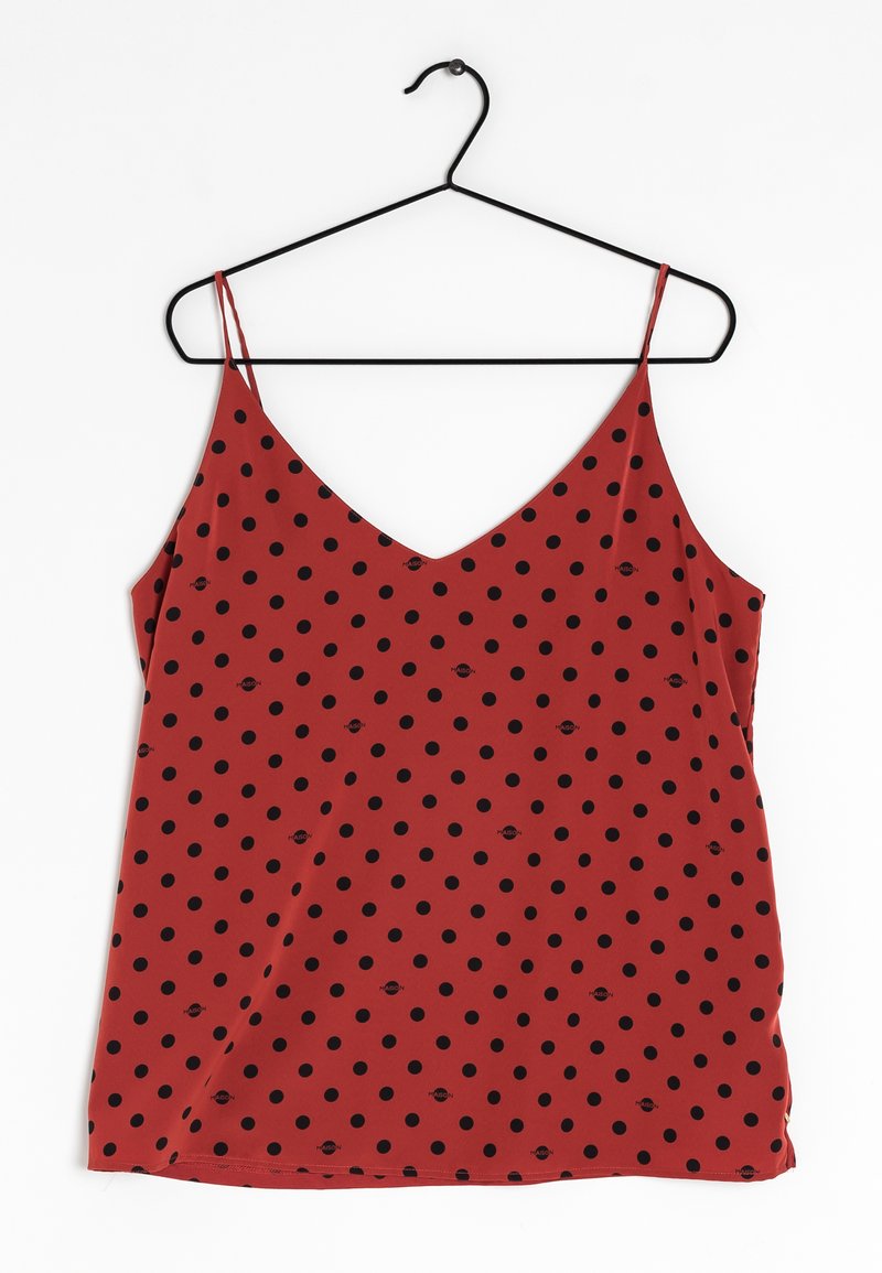 Blouse sans manches rouge en V avec des fines bretelles et des pois noirs, suspendue à un cintre noir sur fond blanc.
