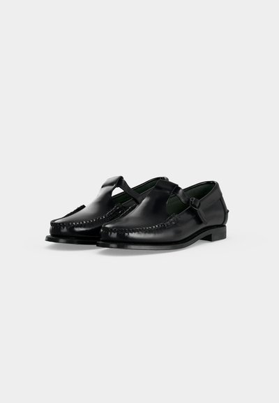 Mocassins Mary Jane en cuir noir à bout rond, détails cousus et une seule bride latérale avec boucle, présentés sur fond blanc.
