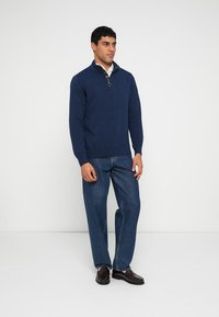 Navy knitted pullover with a quarter-zip collar, paired with straight-leg denim jeans and dark shoes. Simple design, no visible patterns.