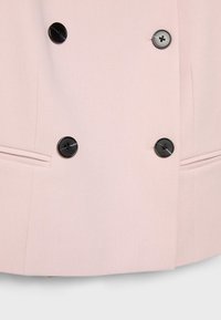 Pale pink double-breasted coat section with four black buttons and two horizontal slit pockets.