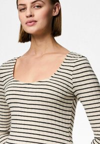 Top a maniche lunghe a maglia rigata di colore crema, con sottili strisce nere, scollo quadrato e silhouette aderente in tessuto strutturato.