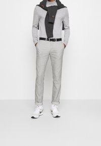 Jasnoszary golf, ciemnoszary dziany szalik, jasnoszare spodnie, czarny pasek i białe sneakersy z czarnymi akcentami. Casualowy, dopasowany wygląd.