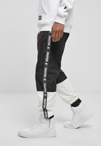 Svartvita joggers med en avsmalnande design, med sidostråkar som har "STARTER"-logotypen. Kombineras med vita högskurna sneakers.
