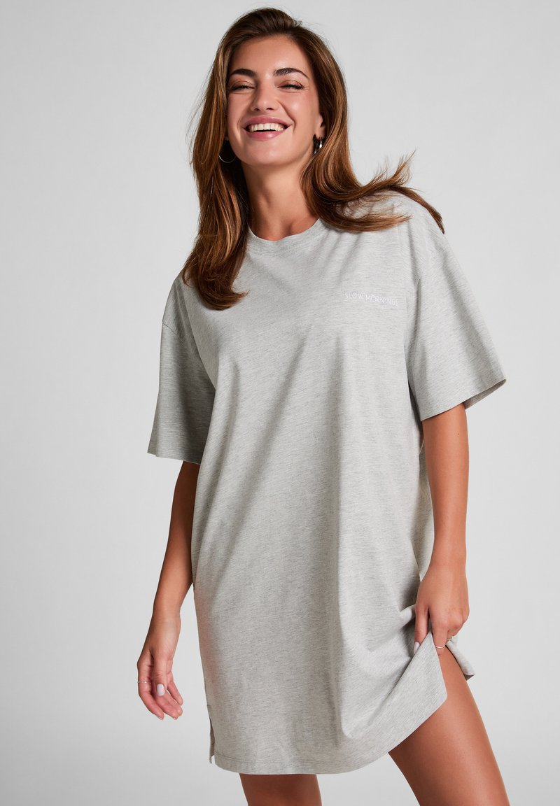 Grau oversize T-Shirt Kleid aus weichem Stoff, mit kurzen Ärmeln und einem kleinen gestickten Text auf der Brust, sowie seitlichen Schlitzen am Saum.