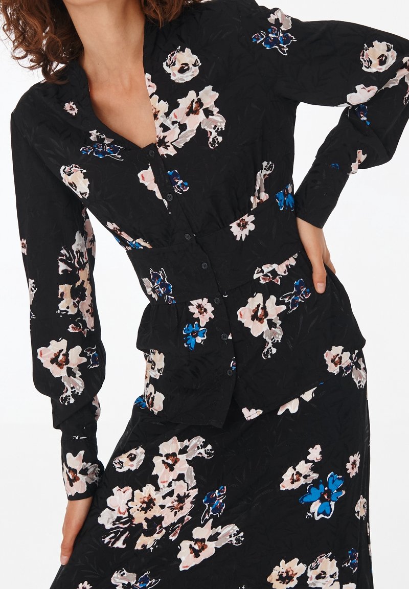 Black floral blouse featuring long sleeves, a button-down front, and a fitted waist. Floral pattern includes pink and blue hues.