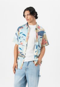 Cămașă cu mâneci scurte, cu nasturi, de culoare bleu deschis, cu modele abstracte în roșu, bleumarin și bej. Purtați peste un tricou alb, combinată cu blugi bleu deschis.