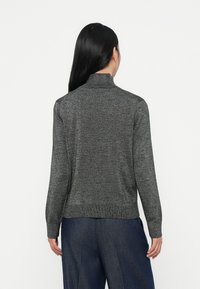 Suéter cinza metálico de gola alta com mangas longas e uma cintura ajustada, usado sobre calças azul-escuras; textura suave.