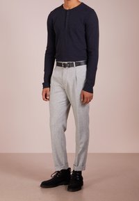 Navy long-sleeve henley shirt with two buttons; light gray tailored trousers; black belt; black suede boots; relaxed fit.
