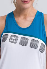 Canotta caratterizzata da una sezione superiore blu, una sezione inferiore bianca con motivi a righe orizzontali e un dettaglio del logo grigio sul davanti.