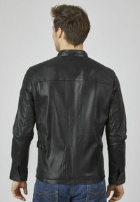 Giacca in pelle nera aderente, con dettagli trapuntati sulle spalle e colletto alto. Texture liscia e linee pulite.