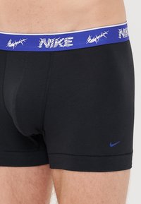 Fekete pamut boxer alsónemű, kék elasztikus derékkal, amelyen fehér "Nike" felirat található. A szár alsó részén egy kis kék Nike logó is látható.