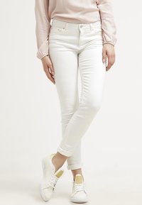 Witte denim jeans met een slim fit en een lichte stretch, gecombineerd met witte sneakers met gele accenten en een textuur op het achterpaneel.