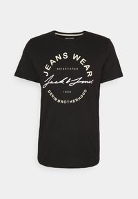 Camiseta negra de algodón con escote redondo y mangas cortas. La gráfica del frente muestra "JEANS WEAR" y "Jack & Jones" en blanco y crema.