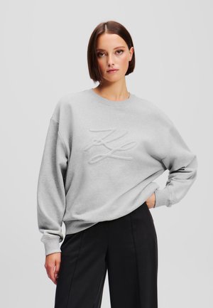 Sweatshirt gris clair avec un logo brodé texturé sur le devant. Présente un col ras du cou et une coupe oversized, fabriqué à partir d'un tissu doux.