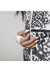 Svartvit leopardmönstrad jacka med dragkedja, utrustad med tumhål i mudden och blanka detaljer. Slät textur och modern design.