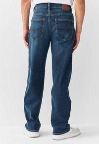 Mörkblå denimjeans med avslappnad passform, med en brun läderlapp vid midjan och kontrasterande sömmar på bakfickorna.
