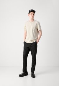 Beige T-shirt med kort ärm och "BOSS"-logga, kombinerad med svarta byxor och svarta snörskor, bärs med en svart keps. Minimalistisk design.