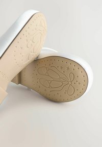 Bailarinas de satén blanco con un acabado suave. La suela de goma texturizada presenta un diseño de zapatilla de ballet y patrones de estrellas.