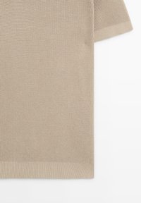 Haut beige en tricot avec un motif texturé, manches courtes et ourlet côtelé. Le tissu a une apparence légèrement structurée.