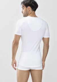 Chemise blanche à manches courtes en tissu lisse, au design ajusté, avec un col rond et un dos sans couture pour plus de confort. Portée avec un short blanc assorti.