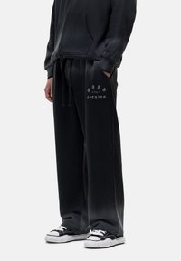 Zwarte sweatpants met een koord in de taille, relaxte pasvorm en de tekst "GID for Nothing" gedrukt op de linker bovenbeen. De stof lijkt zacht en gestructureerd.