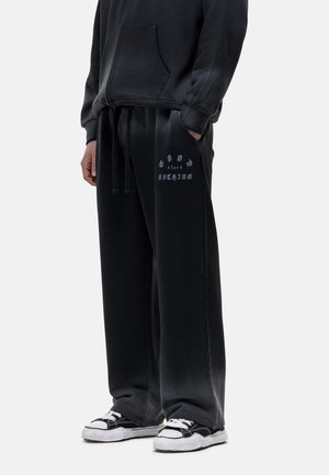 Zwarte sweatpants met een koord in de taille, relaxte pasvorm en de tekst "GID for Nothing" gedrukt op de linker bovenbeen. De stof lijkt zacht en gestructureerd.
