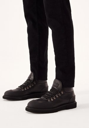 Bottes de randonnée noires avec une tige en cuir lisse, œillets en métal et capuchon renforcé. Semelle en caoutchouc pour une traction et une durabilité accrues.