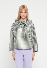 Zielono-biała krótka kurtka w kratkę gingham z dużym falbankowym kołnierzem, regulowanym ściągaczem i elastycznymi akcentami. W połączeniu z lawendowymi spodniami z sztruksu.
