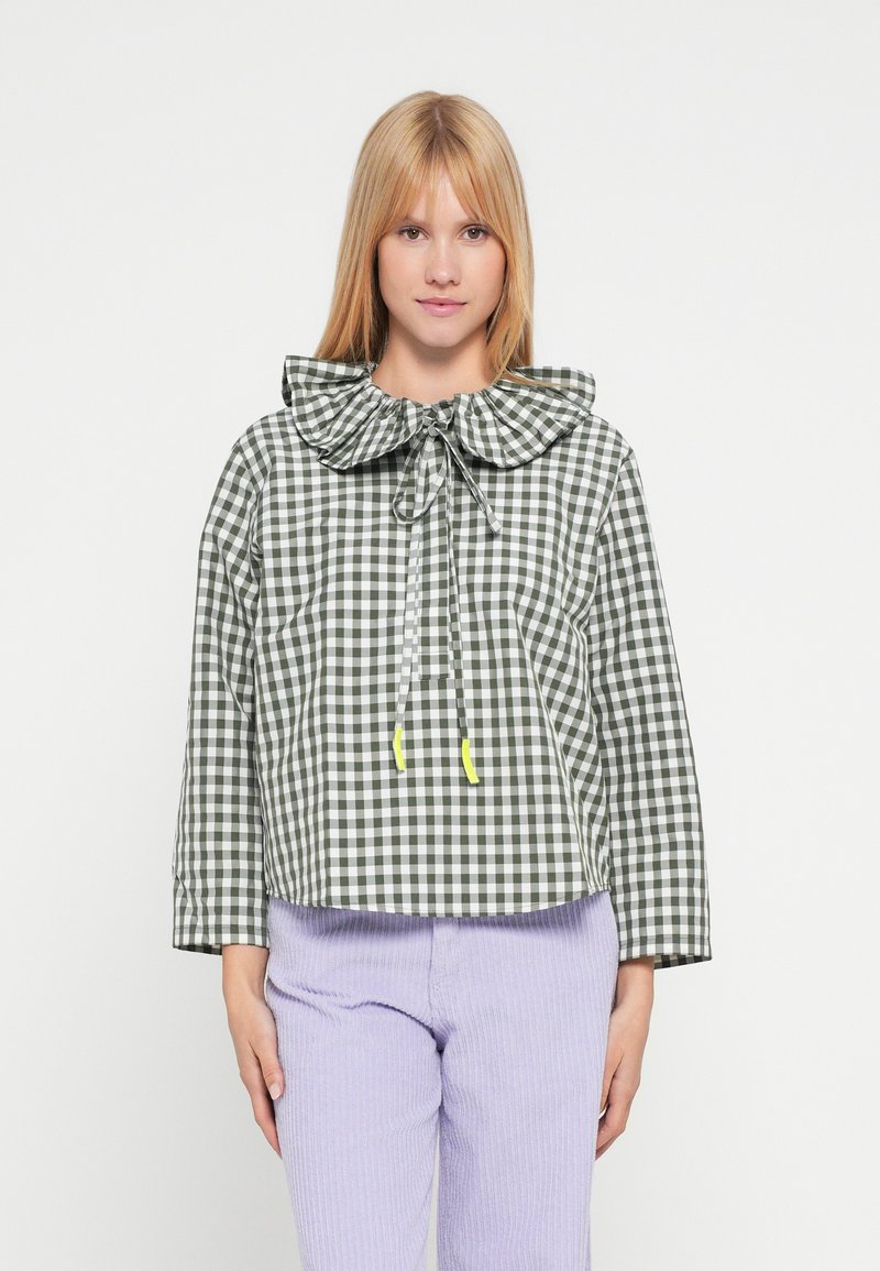 Zielono-biała krótka kurtka w kratkę gingham z dużym falbankowym kołnierzem, regulowanym ściągaczem i elastycznymi akcentami. W połączeniu z lawendowymi spodniami z sztruksu.