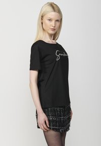 Camiseta de algodón negra de manga corta y cuello redondo, con letras de strass plateado en el pecho.