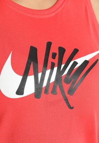 Débardeur de sport rouge avec un grand swoosh Nike blanc et un texte "Nike" noir stylisé imprimé sur la poitrine.