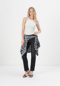 Tricou gri, blugi negri și o cămașă albastră în carouri legată la talie. Sandale negre cu toc înalt și buline albe. Fundal alb.