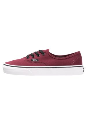 Zapatilla Vans de caña baja color granate con cordones negros y suela de goma blanca, vista desde un lateral que muestra la etiqueta de la marca y detalles de costura.