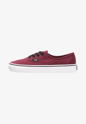 Zapatilla Vans de caña baja color granate con cordones negros y suela de goma blanca, vista desde un lateral que muestra la etiqueta de la marca y detalles de costura.