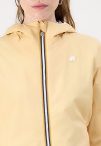 Giacca gialla con cappuccio realizzata in tessuto leggero, con zip frontale e strisce multicolori, e un logo discreto sul petto.