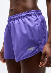 Ανδρικός κορμός και χέρι που φορούν μωβ σορτς τρεξίματος New Balance με ελαστική μέση, σε λευκό φόντο.