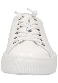 Baskets blanches avec une surface lisse et brillante, bout rond et semelle plate en caoutchouc. Possède des œillets métalliques, des lacets et des détails de couture subtils.